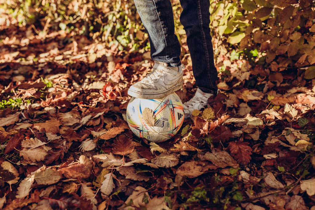 Ein Kind steht mit einem Fußball im herbstlichen Laub