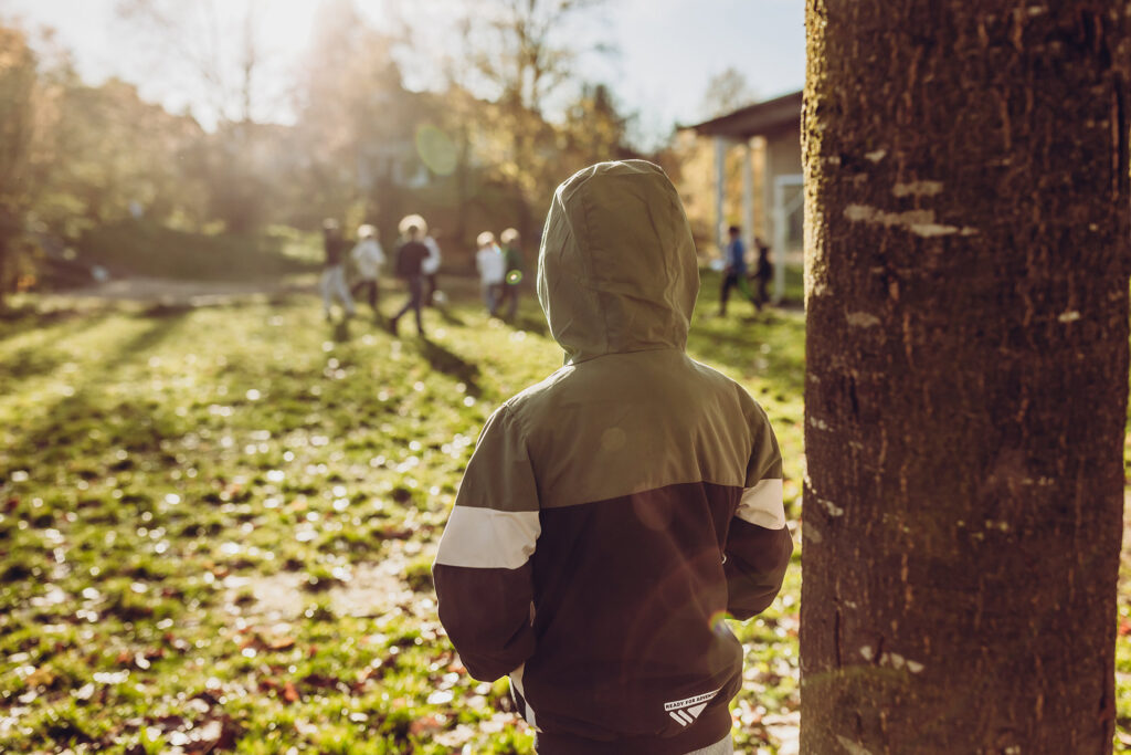 Ein Kind steht am Baum und schaut über den Schulhof