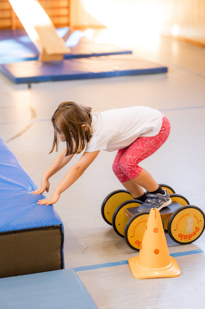 Kind balanciert über ein Sportgerät in der Turnhalle