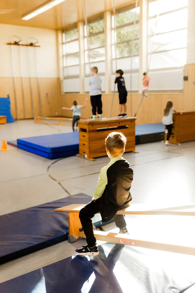 Kind springt von einem Kasten in der Turnhalle