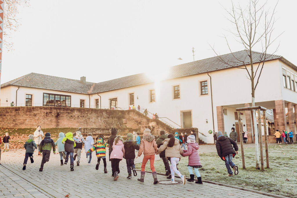 Kinder bewegen sich gemeinsam auf dem Schulhof vor dem Schulgebäude