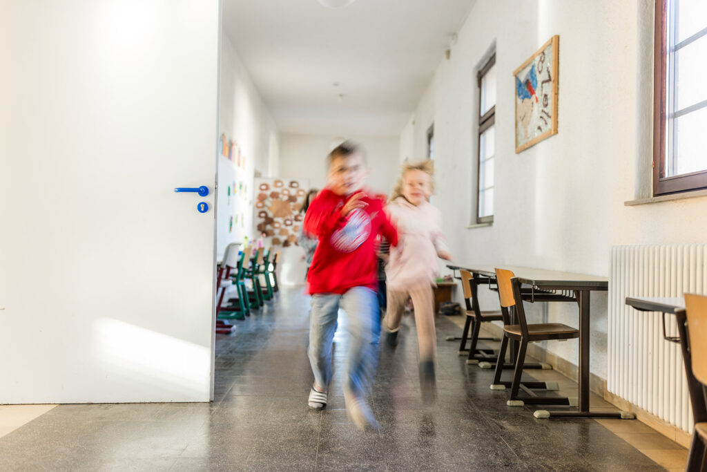 Zwei Kinder laufen durch einen Flur im Schulgebäude