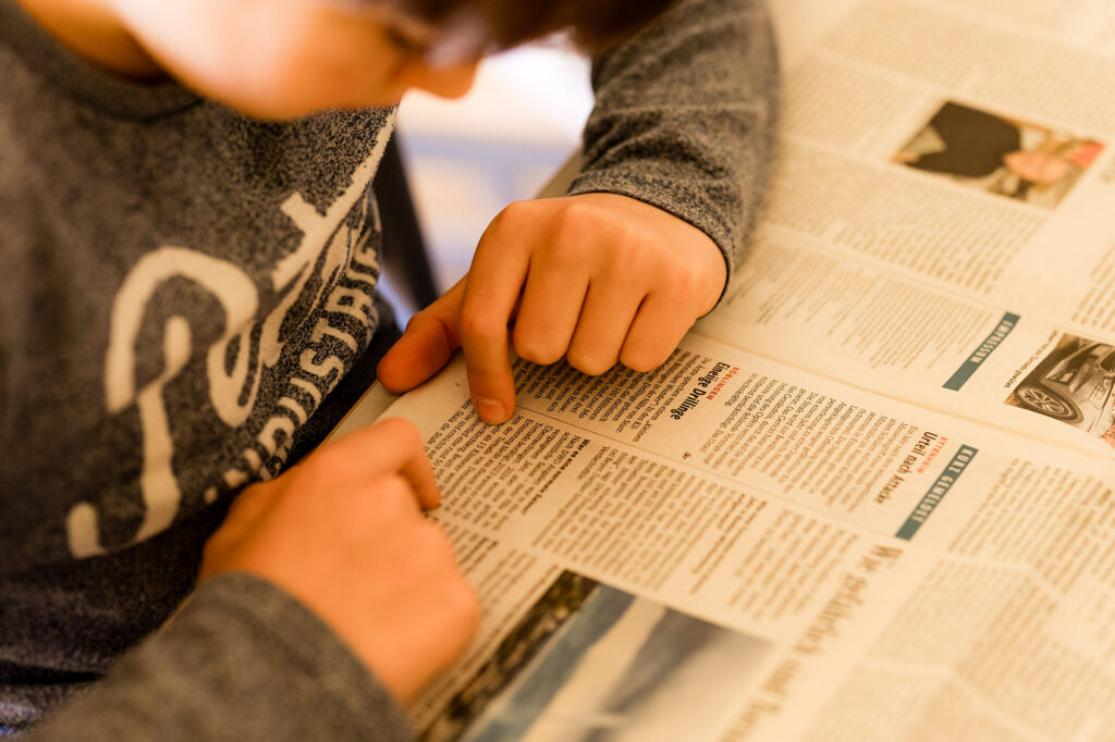 Kind zeigt auf einen Text in einer Zeitung